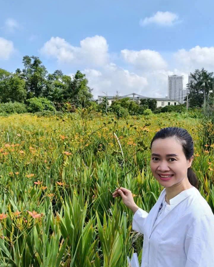 Nguyễn Hoa mặc áo trắng đứng cạnh cánh đồng hoa trong buổi thực tế vườn dược liệu